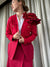 Blazer rojo intenso de manga largas con detalle de bolsillos y botones dorados. Una flor diseñada en capas decora el hombro izquierdo ideal para un look corporativo moderno.